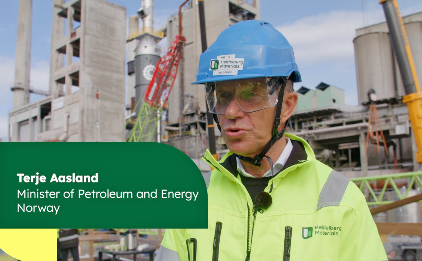 A man in a high-visibility jacket and hard hat stands in front of industrial machinery, with the name ‘Terje Aasland, Minister of Petroleum and Energy Norway’ displayed on a label.